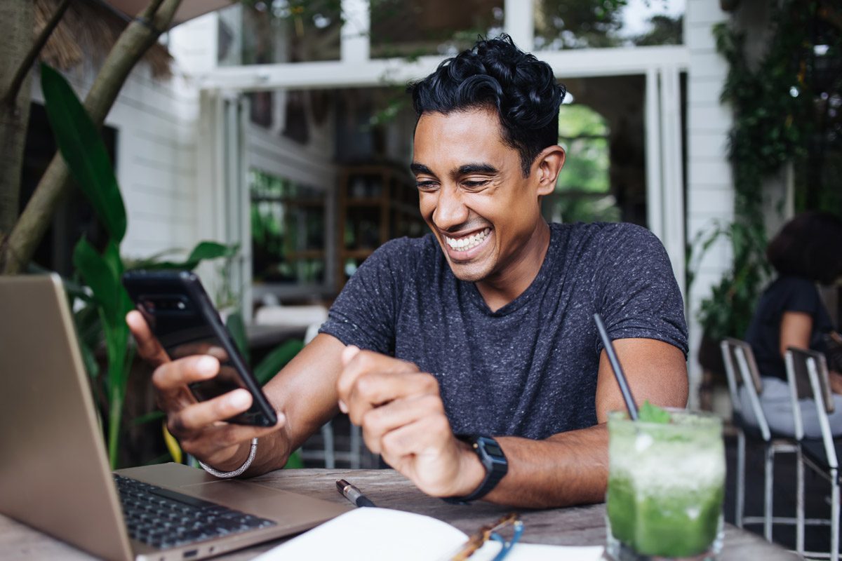 Hispanic Adult Man Having Fun While Interacting With Smartphone On Terrace
